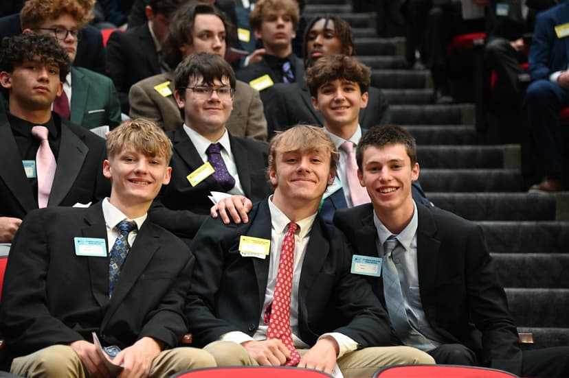 Three students in suits smiling at an evening assembly